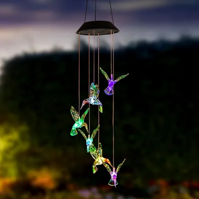 A solar-powered wind chime with hummingbird-shaped lights hanging outdoors at dusk.