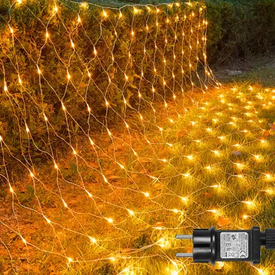 A net of yellow lights is draped over bushes and spread across the grass in a garden setting.