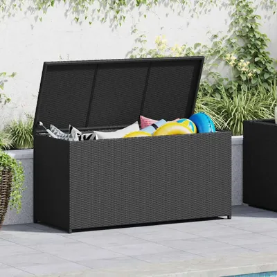 An open black poly rattan storage box filled with colorful cushions and pool floats, placed on a tiled patio next to a swimming pool.