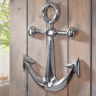 A shiny silver anchor decoration mounted on a wooden plank wall.