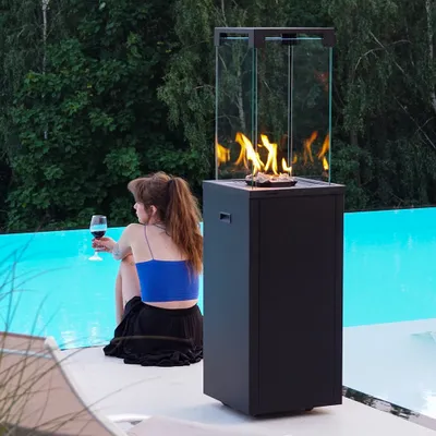 A woman sits by a pool with a glass of wine next to a modern outdoor gas fireplace.