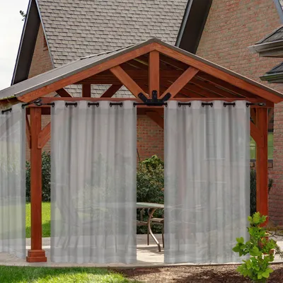 Outdoor curtains hanging on a wooden gazebo with a table and chairs visible inside.