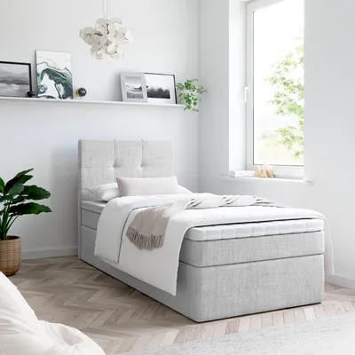 A bedroom scene with a bed, a plant, and artwork on the wall.