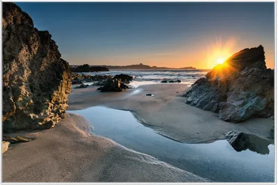 Produktbild von Wallario Wandbild Sonnenuntergang hinter einem Felsen am Strand, Größe: 61 x 91,50 cm, Poster mit weißem Aluminiumrahmen