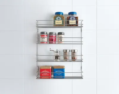 A metal spice rack mounted on a white tiled wall, filled with various spices and tea tins.