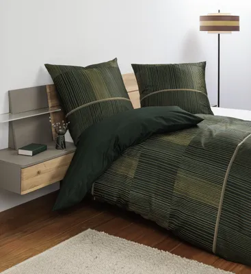 A bedroom scene with a bed featuring green and gold striped bedding, a nightstand with a book and vase, and a floor lamp in the background.