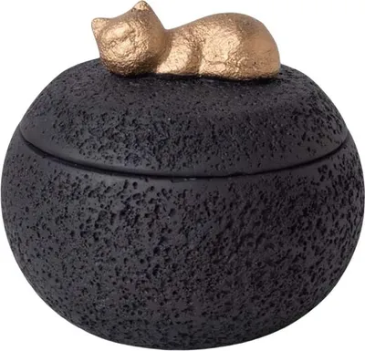 A black, textured, round lidded container with a gold cat figurine on top.