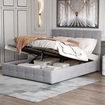 A bedroom scene with a bed that has its storage compartment open, revealing storage boxes inside. The bed is made with bedding and a throw blanket.
