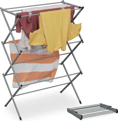 A collapsible drying rack with clothes on it, and a folded drying rack on the floor.