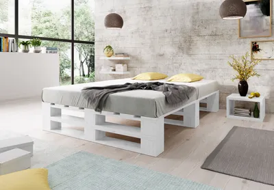 A bedroom scene featuring a white pallet bed with bedding, a nightstand, and decorative elements.
