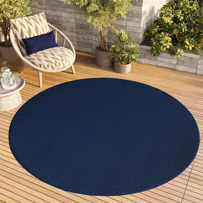 A round navy blue rug on a wooden deck with a chair and potted plants.