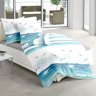 A bed with bedding featuring a coastal wave and bird design, set in a room with a balcony visible in the background.
