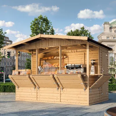 A wooden market stall selling baked goods and coffee, set up on a paved plaza with buildings and trees in the background.