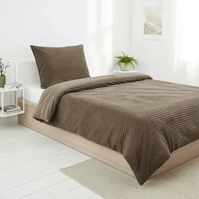 A neatly made bed with taupe bedding in a bright room.