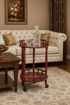 A wooden bar cart with a decanter and glass on it, placed in a living room setting next to a sofa.