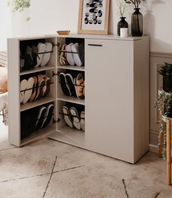 A shoe cabinet filled with shoes, placed in a room with a rug and some decor.