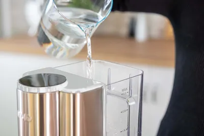 Jemand gießt Wasser aus Glaskrug in Unold Express Ava aus durchsichtigem Kunststoff auf Küchentheke.
