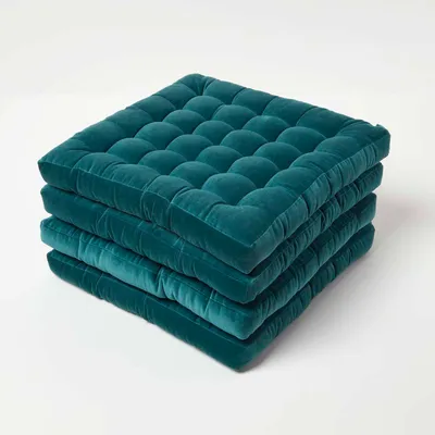 A stack of four teal velvet seat cushions on a white background.