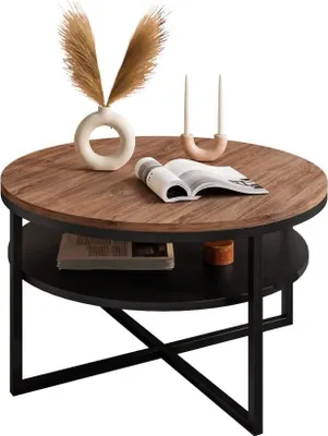 A round coffee table with a wooden top and black metal legs, decorated with a vase of dried flowers, a candle holder with candles, and an open book.