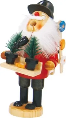 Räuchermännchen mit Bauchladen schwarzen Hut roten Mantel eine Kiste mit zwei kleinen Topfpflanzen.
