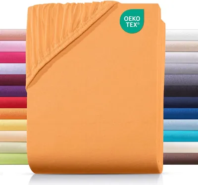 A folded orange fitted sheet is shown with a stack of other colored sheets in the background. A green OEKO-TEX logo is visible in the top right corner.