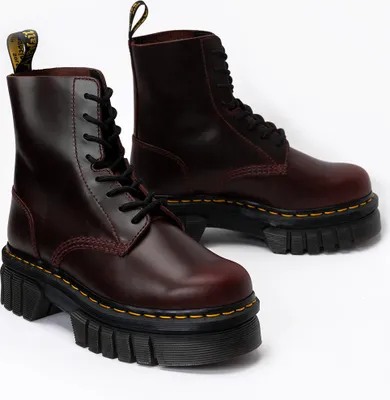 A pair of burgundy Dr. Martens boots with thick black soles are shown against a white background.