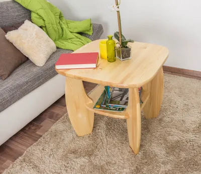 A wooden coffee table with a book, a plant, and a yellow vase on it, placed next to a sofa with a green blanket and pillows.