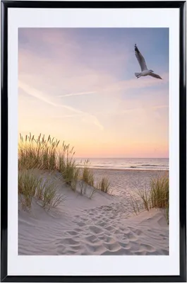 A framed picture of a beach scene with a seagull flying in the sky.