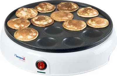 A close-up, slightly angled view of a white poffertjes maker with mini pancakes cooking on its surface.