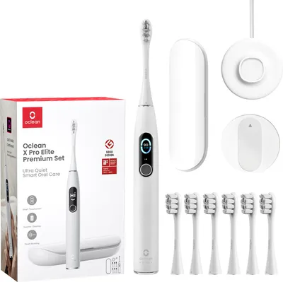A white Oclean X Pro Elite Premium Set electric toothbrush and its accessories are displayed on a white background. The set includes the toothbrush, a charging base, a travel case, and multiple brush heads. The packaging box is also visible on the left sid