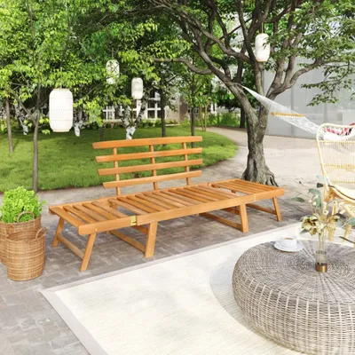 A wooden garden bench and lounge chair set in a lush garden setting with trees, grass, and lanterns.