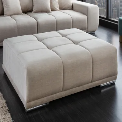 A square ottoman sits on a dark floor in front of a sectional sofa.