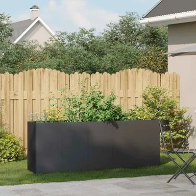 A black rectangular planter filled with plants sits on a green lawn in a backyard setting, with a wooden fence and a house in the background.