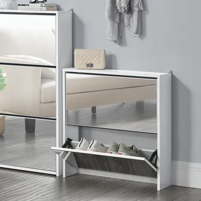A white shoe cabinet with mirrored doors is shown in a room with a gray wall and wooden floor. A cream-colored handbag is placed on top of the cabinet.
