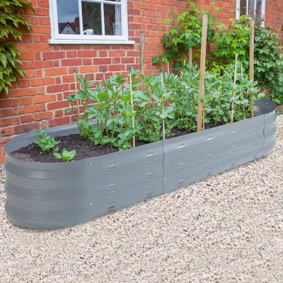 A raised garden bed filled with plants, situated next to a brick house.