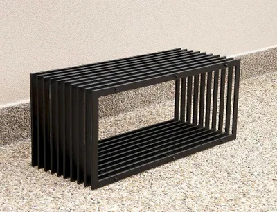 A black metal bench is placed on a gravel and concrete surface next to a light-colored wall.
