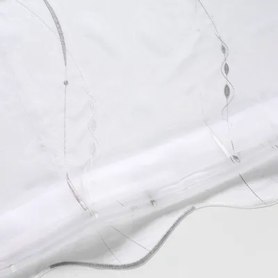 A close-up view of a white and silver roller blind, showing its textured fabric and decorative stitching.