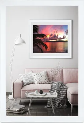 A living room scene with a pink sofa, a coffee table, and a framed picture of a sunset over the ocean.