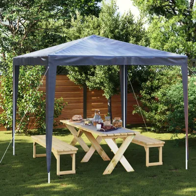 A party tent set up in a garden with a picnic table and benches.