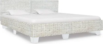 A white rattan bed with white pillows and a white mattress.