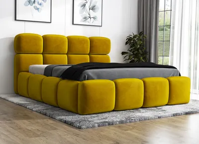 A yellow upholstered bed with a gray comforter and black throw blanket is shown on a gray rug in a room with artwork on the wall and a plant near a window.
