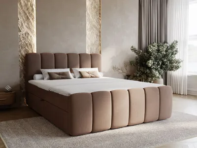 A bedroom scene with a large, upholstered boxspring bed as the focal point, decorated with pillows and a throw. The room features textured walls, curtains, and a plant.