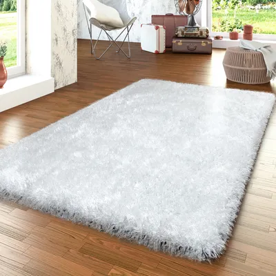 A white shag rug is placed on a wooden floor in a room with a window and some decorative items.