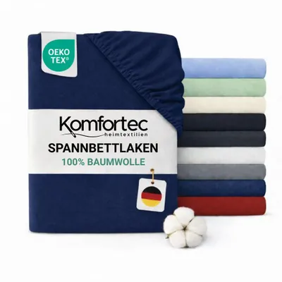 A folded navy blue fitted sheet is shown in the foreground, with a stack of fitted sheets in various colors in the background. A cotton boll is also visible.