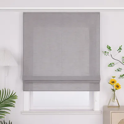 A gray Roman blind is installed on a white window frame, with a lamp on the left and a vase with flowers on the right.