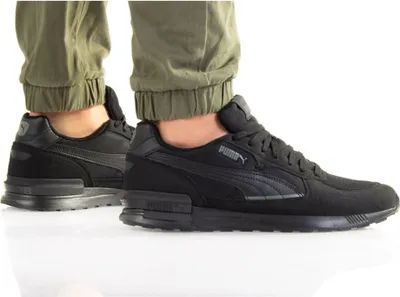 A person wearing black Puma sneakers and green pants, shown from the ankle down.