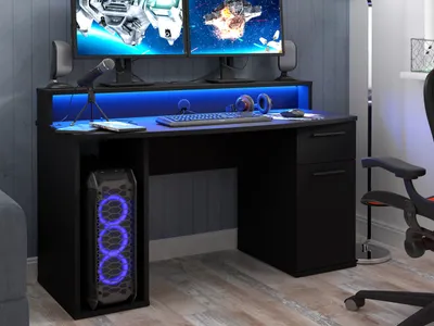 A black gaming desk with dual monitors, a keyboard, headphones, and a computer tower with blue RGB lighting.