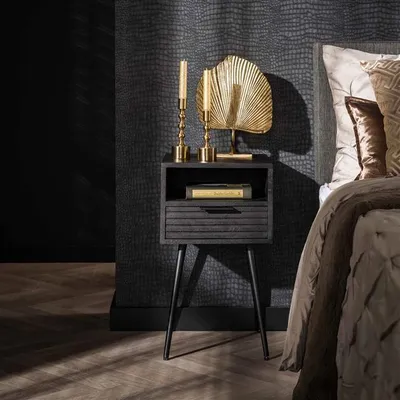 A dark, moody bedroom scene featuring a black bedside table with gold decorative items and a book, next to a bed with textured bedding.