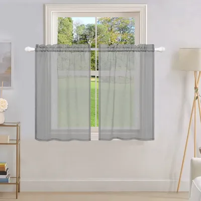 A window with sheer gray curtains hanging over it, with a view of trees and grass outside.