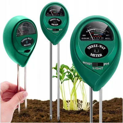 Three green soil meters are shown inserted into brown soil, with small green plants growing nearby. A hand is shown holding one of the meters.